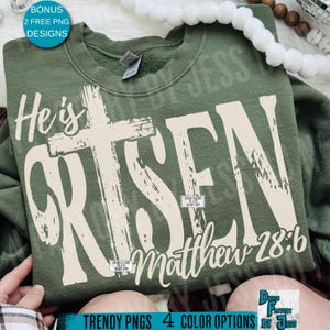 May include: An olive green sweatshirt with the words "He is Risen" in a distressed, off-white font, with a cross graphic. The text "Matthew 28:6" is below. The image also includes text that says "Trendy PNGs 4 Color Options by Jess".