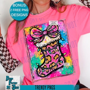 May include: A pink long-sleeved shirt with a graphic of a Christmas stocking with a leopard print design, a bow, and string lights. The image has the text "TRENDY PNGS" and "BONUS 2 FREE PNG DESIGNS".
