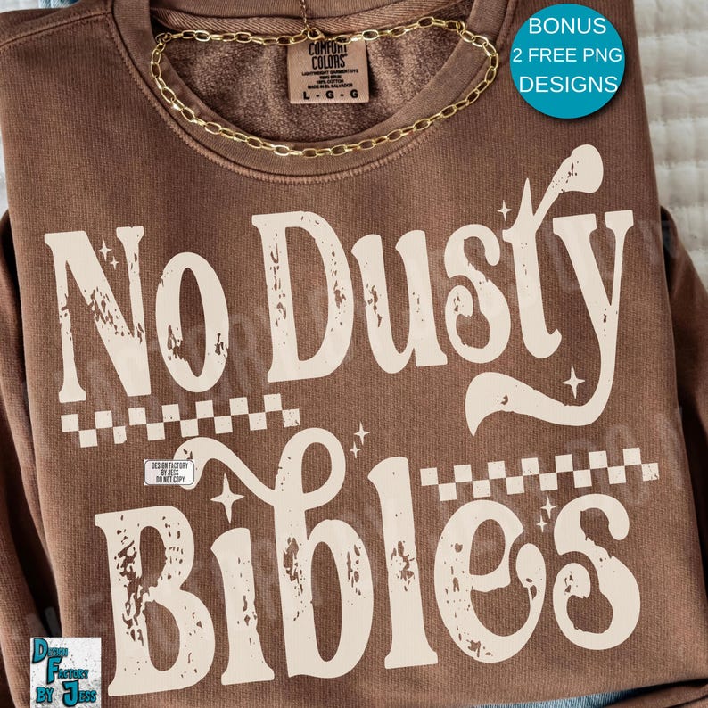 May include: A brown sweatshirt with the text "No Dusty Bibles" in a distressed, off-white font. The design includes a checkered pattern and stars. A gold chain necklace is draped across the top. The sweatshirt has a tag that says "Comfort Colors".