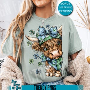 May include: A light green t-shirt featuring a cartoon Highland cow with a blue plaid bow, hat, and scarf, adorned with shamrocks. The text "BONUS 2 FREE PNG DESIGNS" is in a blue circle. The bottom of the shirt has the text "TRENDY PNGS".