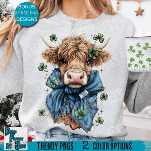 May include: A light grey sweatshirt with a watercolour illustration of a Highland cow wearing a blue scarf and shamrocks. The image includes text that reads "BONUS 2 FREE PNG DESIGNS" and "TRENDY PNGS 2 COLOR OPTIONS". A white mug with shamrocks is also visible.