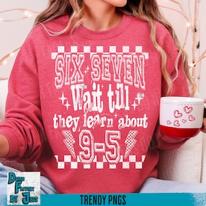 May include: A red sweatshirt with the text "SIX SEVEN Wait till they learn about 9-5" in white. The sweatshirt has a crew neck and long sleeves. A white mug with red hearts is held in the hand.