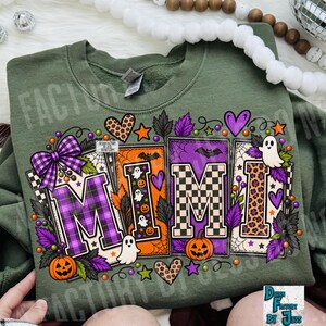 May include: An olive green sweatshirt featuring a graphic print of the word MIMI in large block letters. The letters are decorated with purple plaid, orange ghost patterns, black and white checkers, and leopard print, surrounded by pumpkins and ghosts.