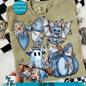 May include: A light green Comfort Colors t-shirt featuring a whimsical Halloween design. The design includes a blue bat holding a pumpkin, a ghost with a broom, and a blue pumpkin with a bow. The shirt also has the text "BONUS 2 FREE PNG DESIGNS" and "TRENDY PNGS".