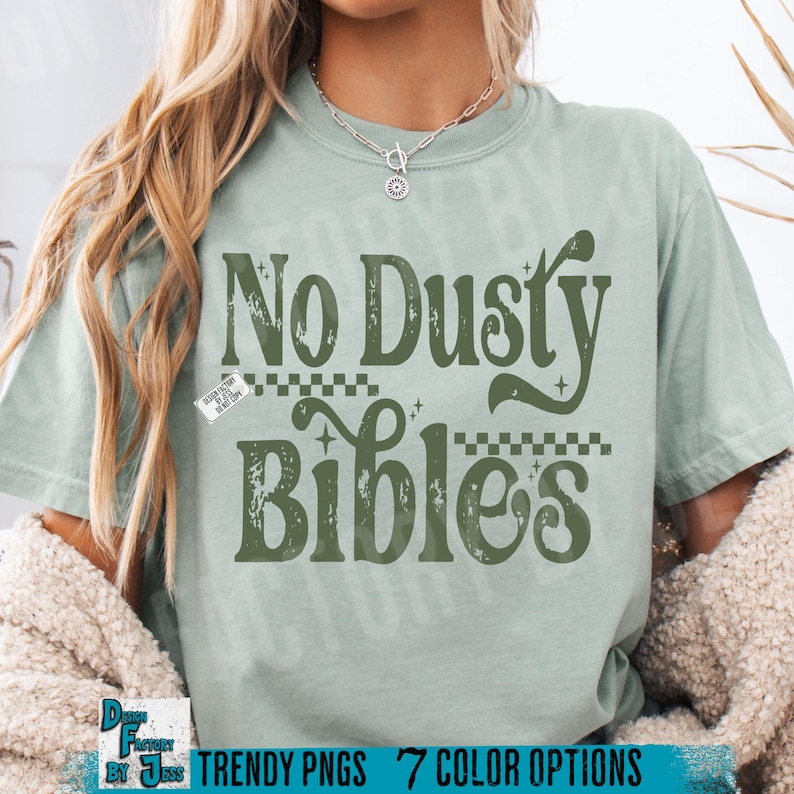 May include: A light green t-shirt with the text "No Dusty Bibles" in a retro font. The design includes decorative elements and is printed in a darker green color. The shirt has a relaxed fit.