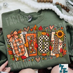 May include: An olive green crewneck sweatshirt featuring a graphic print that spells GIGI. Each letter is framed in a rectangular border decorated with autumn leaves, sunflowers, hearts, stars, and patterns including plaid, floral, and leopard print.