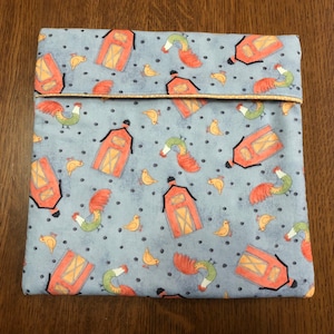 May include: A blue fabric pouch with a repeating pattern of red barns, roosters, and yellow chicks. The pouch has a yellow seam around the top edge.