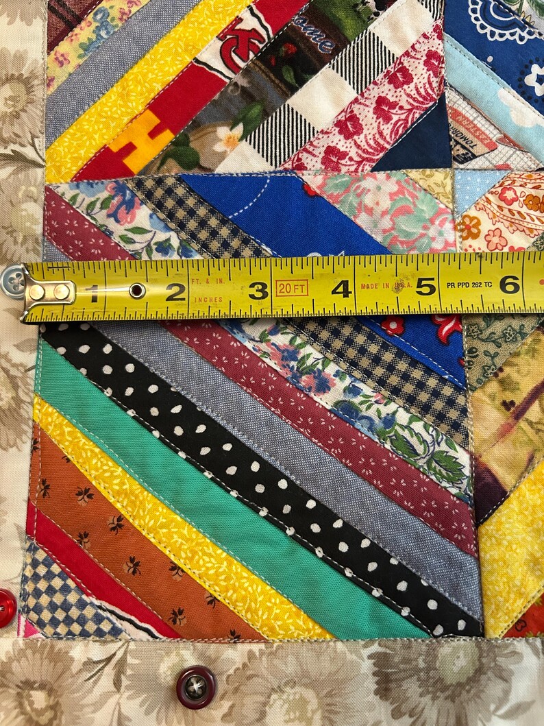 May include: A multicolored fabric quilt featuring diagonal strips of various patterns including polka dots, florals, and solid colors. A yellow measuring tape is placed across the quilt, showing a width measurement of approximately 6 inches.