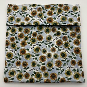 May include: A light blue fabric item with a repeating pattern of sunflowers and the word "Sunflower" in a script font. The sunflowers are yellow and brown with green leaves.