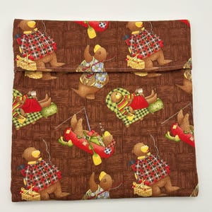 May include: A rectangular fabric pouch featuring a brown background with a woven texture pattern. The fabric is printed with repeating illustrations of brown bears engaged in outdoor activities like fishing, rowing a red canoe, and relaxing.