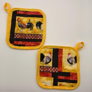 May include: Two square fabric pot holders featuring a yellow background with a rooster print, black vertical and horizontal bands, and a red and brown checkered pattern. Each pot holder has a yellow fabric border and a small loop for hanging.