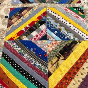 May include: A quilted table runner featuring a patchwork design of diagonal fabric strips in various colors and patterns, including floral, polka dot, and plaid prints. The quilt includes text reading GO VOTE and Sunflower, accented by buttons.