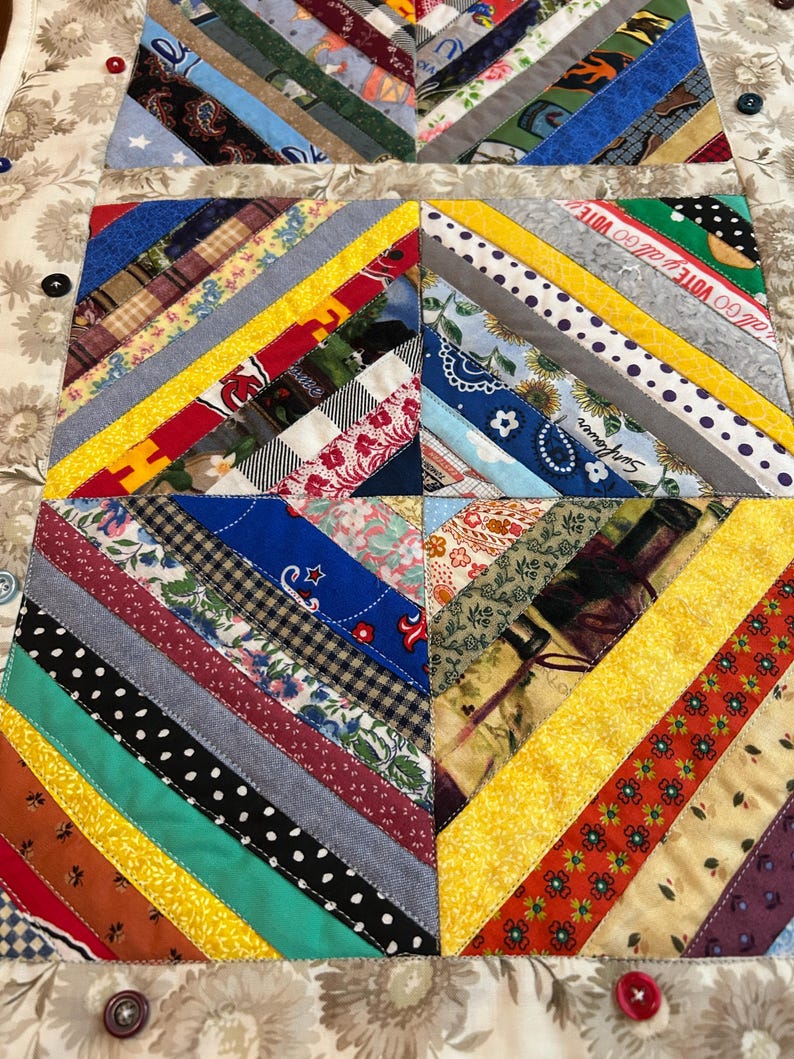 May include: A quilted table runner featuring a patchwork design of diagonal fabric strips in various colors and patterns, including floral, polka dot, and plaid prints. The quilt includes text reading GO VOTE and Sunflower, accented by buttons.