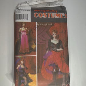 May include: A Simplicity Costumes sewing pattern package featuring images of vintage costume designs. The package includes illustrations of women in elaborate dresses and outfits, with the text "Simplicity Costumes" in orange.