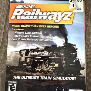 Puede incluir: Caja de DVD para PC del juego Trainz Railwayz. La portada presenta una imagen en blanco y negro de un tren de vapor con humo. El texto incluye "MORE TRAINZ THAN EVER BEFORE!" y "THE ULTIMATE TRAIN SIMULATOR!"