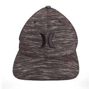 May include: A baseball cap featuring a dark grey and white heathered fabric pattern. The front panel displays a black embroidered logo consisting of two curved shapes facing each other. The cap has a structured crown and a curved brim.