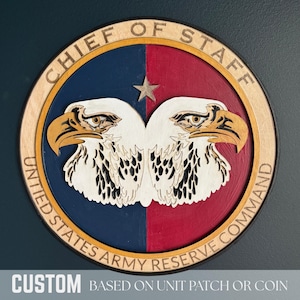 May include: Wooden plaque featuring the words "CHIEF OF STAFF" and "UNITED STATES ARMY RESERVE COMMAND". The design includes two eagles, a star, and text that reads "CUSTOM BASED ON UNIT PATCH OR COIN". The plaque is round with a blue, red, and natural wood color scheme.