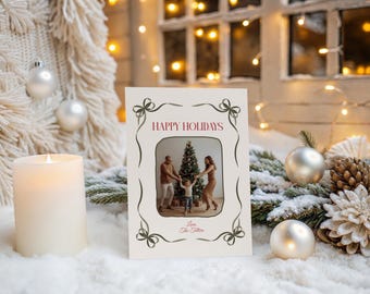 May include: A holiday greeting card with a family photo inside a decorative frame. The card reads "HAPPY HOLIDAYS" in burgundy lettering, with a bow design. The scene includes a lit candle, ornaments, and pine cones.