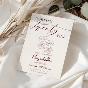 Puede incluir: Una tarjeta de invitaci&oacute;n color crema con texto e ilustraciones en borgo&ntilde;a. La tarjeta dice "Turning Twenty Fine" e incluye detalles para una celebraci&oacute;n de cumplea&ntilde;os n&uacute;mero 25, con dos copas de c&oacute;ctel. Flores secas decorativas y tela en el fondo.