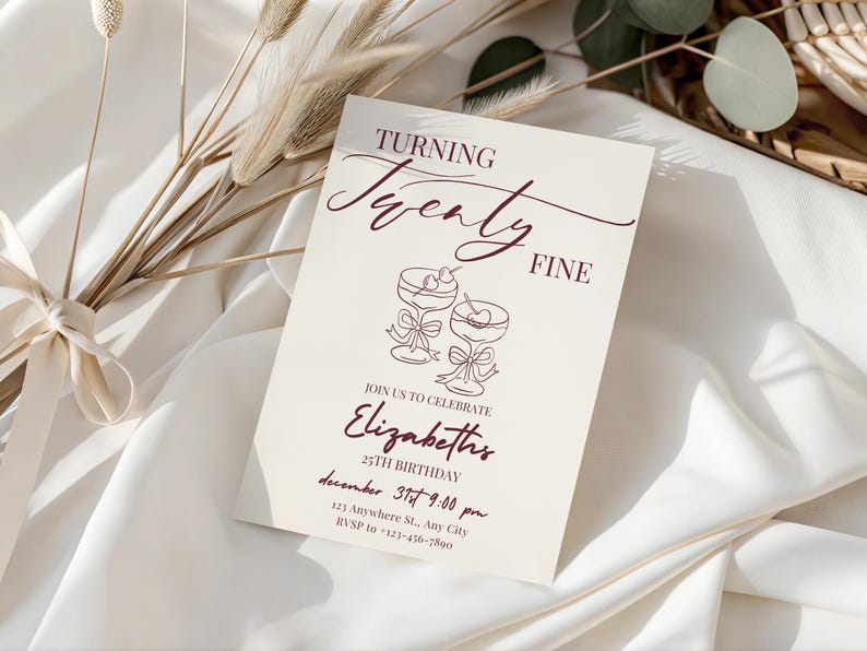Puede incluir: Una tarjeta de invitaci&oacute;n color crema con texto e ilustraciones en borgo&ntilde;a. La tarjeta dice "Turning Twenty Fine" e incluye detalles para una celebraci&oacute;n de cumplea&ntilde;os n&uacute;mero 25, con dos copas de c&oacute;ctel. Flores secas decorativas y tela en el fondo.