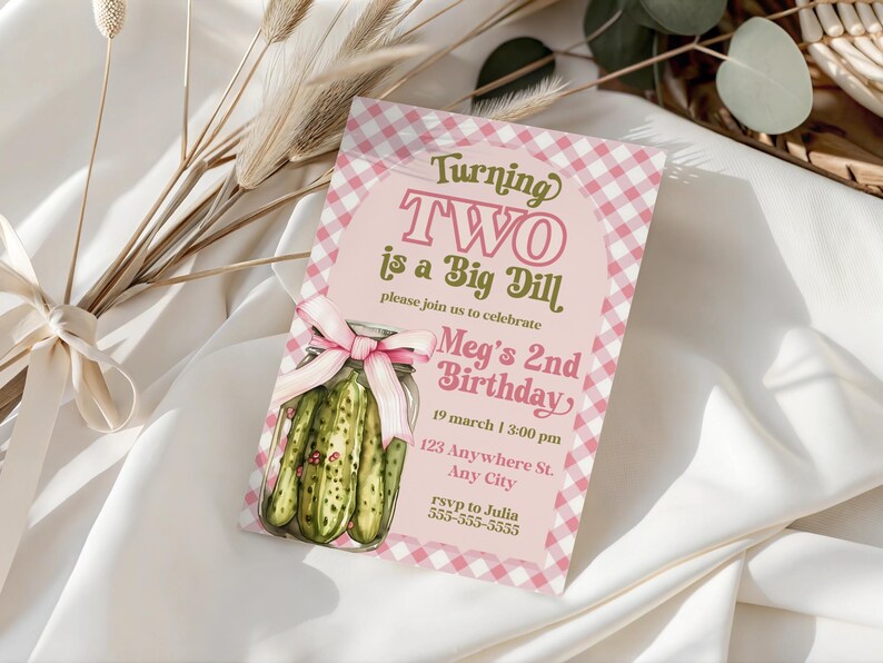 May include: A pink and white gingham birthday invitation with the text "Turning TWO is a Big Dill." The invitation features a jar of pickles and a pink bow. The invitation includes the birthday details.