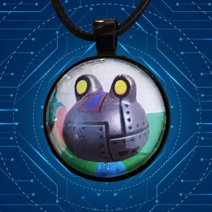 May include: A round pendant necklace featuring a robot frog design. The frog has yellow eyes, a gray body, and a blue and red accent. The pendant hangs from a black cord.