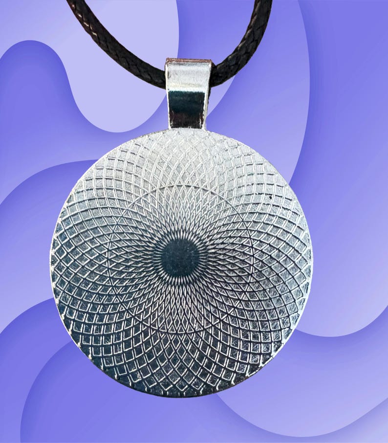 Puede incluir: Primer plano de un colgante plateado con un patr&oacute;n geom&eacute;trico. El colgante redondo est&aacute; unido a un collar de cord&oacute;n negro. El fondo es un degradado de morado y azul.