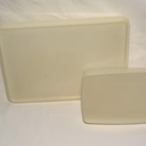 May include: Two off-white rectangular containers, one larger than the other, are positioned on a white surface. The containers have rounded corners and a slightly glossy finish. The larger container is rectangular, while the smaller one is more square.