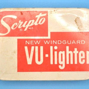 May include: Vintage Scripto VU-lighter in a rectangular case. The case is off-white with a red rectangular section. The text "Scripto" is in white script, and "NEW WINDGUARD VU-lighter" is in red.