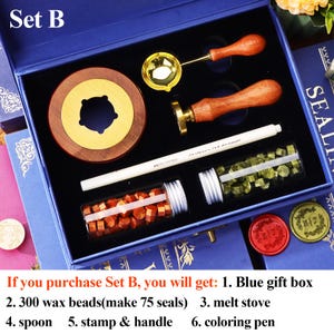 May include: A blue gift box set containing a wax seal kit. The kit includes a wooden and brass wax warmer, a brass stamp with a wooden handle, a spoon, a coloring pen, and two vials of wax beads. The text "Set B" is visible.