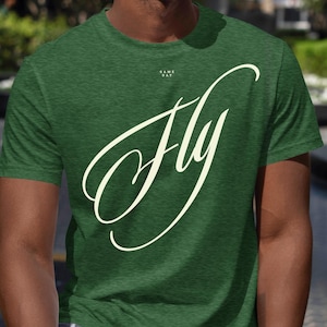 TEE: UNISEX – FLY Football T-Shirt – Bold Typographic Design, Heather Grass Green/Emerald/Black Unisex Tee, Cream dtf Print