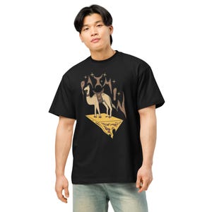 May include: Black t-shirt featuring a camel graphic. The camel is standing on a gold-colored platform with a saddle. Above the camel are brown and gold-colored shapes and stars. The shirt is a relaxed fit.