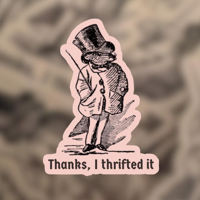 May include: A sticker featuring a vintage illustration of a frog in a top hat and coat, holding a cane. The text "Thanks, I thrifted it" is printed in a serif font at the bottom of the sticker. The sticker has a pink border.