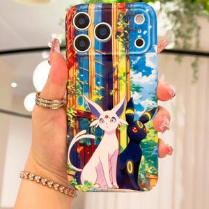 May include: A colourful phone case with an illustration of two Pok&eacute;mon characters, one white and one black, set against a building and sky. The case has a glossy finish and a protective design.