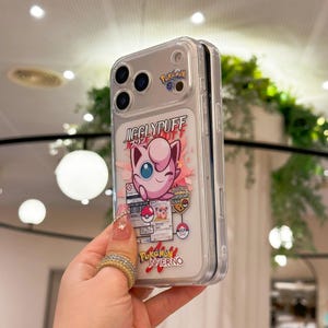 May include: Clear phone case featuring a pink Jigglypuff graphic with the text "JIGGLYPUFF" and "Pokemon Inferno". The case has a clear back and a protective bumper. The design includes other Pokemon-themed graphics.