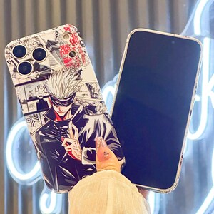 Op de afbeelding: Een telefoonhoesje met een manga-achtige illustratie van een personage met wit haar en een zwarte outfit. De hoes heeft een zwart-wit stripontwerp aan de bovenkant en rode Japanse tekst.