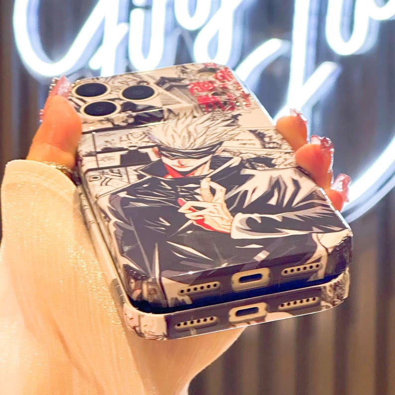 Op de afbeelding: Een telefoonhoesje met een manga-stijl illustratie van een personage met wit haar en een blinddoek, gekleed in een zwarte jas. De hoes heeft een zwart-witte manga-stijl achtergrond met rode accenten. De hoes wordt in een hand gehouden.