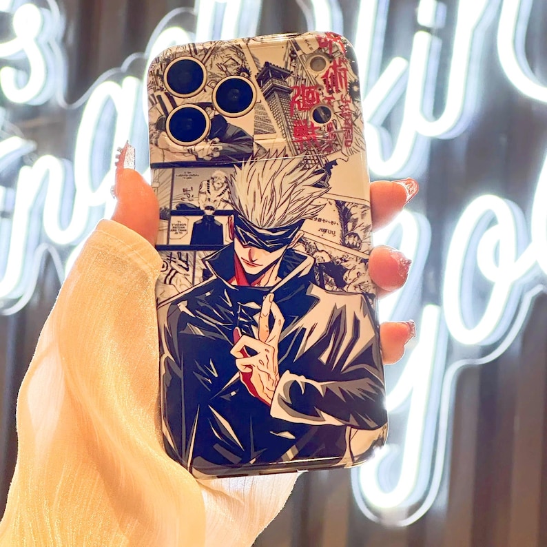 Op de afbeelding: Een wit en zwart telefoonhoesje met een manga-stijl illustratie van een personage met wit haar en een blinddoek. Het ontwerp bevat manga-panelen en Japanse tekst.