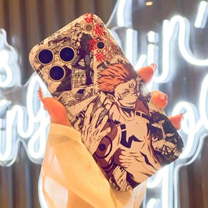 Op de afbeelding: Een witte telefoonhoes met een manga-stijl illustratie van een personage met rood haar en een gedetailleerde zwart-wit achtergrond. De hoes heeft drie cirkelvormige camera-uitsparingen en rode Japanse tekst.