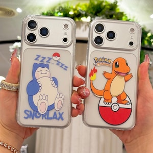 May include: Two clear phone cases with cartoon designs. One features a sleeping blue Snorlax with "Zzz" text, and the other showcases an orange Charmander on a red and white Pok&eacute; Ball. Both cases have a clear border.