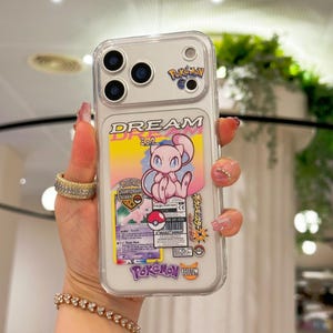 May include: Clear phone case featuring a colorful design with the word "DREAM" and a pink cartoon character. The case also includes a Pokemon card and the words "Pokemon Yellow".