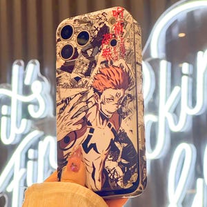 Op de afbeelding: Een telefoonhoesje met een manga-achtige illustratie van een personage met rood haar en tatoeages. De hoes heeft een zwart-wit stripboekontwerp met Japanse tekstaccenten. De hoes wordt in een hand gehouden.
