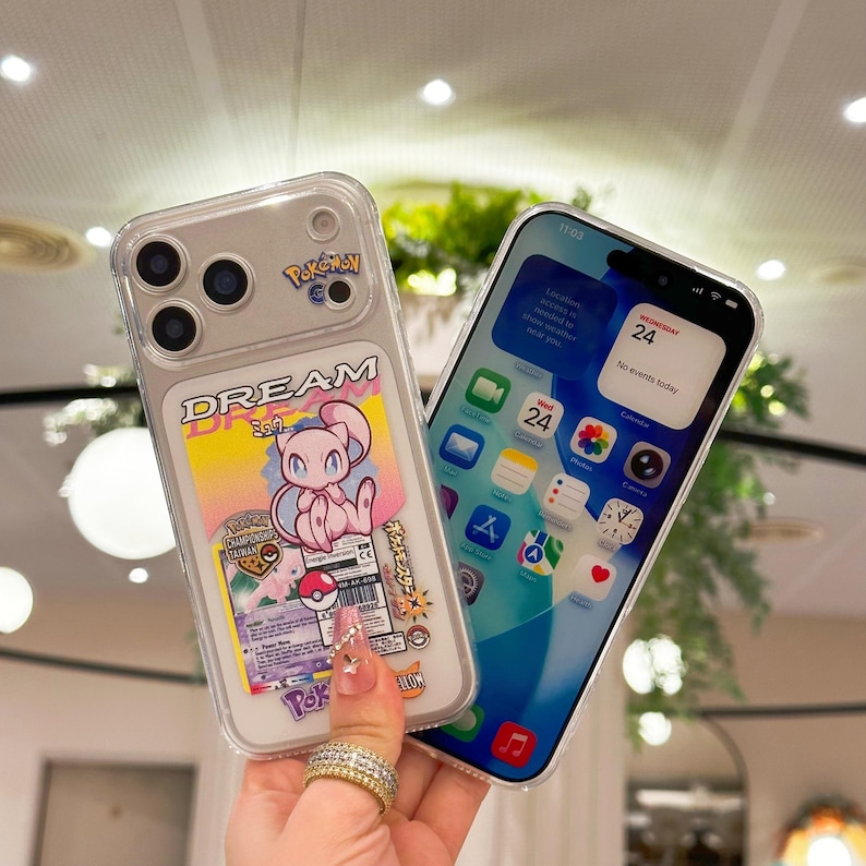 May include: Clear phone case featuring a Pokemon design with a pink Mew character and the word "DREAM". The phone on the right displays a blue and white screen with app icons and the date.