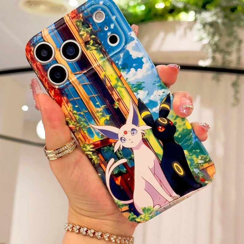 May include: A colourful phone case with an anime-style illustration. The design features a cityscape with blue skies and cartoon characters. The case is held by a hand with jewellery.