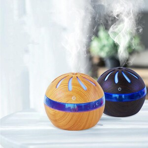 May include: Two spherical essential oil diffusers with a wood grain finish, one light brown and one dark brown. Each features a horizontal blue LED light band, a power button icon, and a top vent emitting a steady stream of white mist vapor.