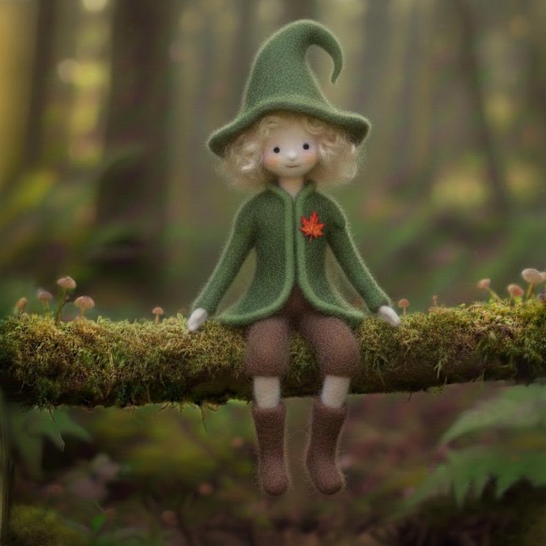 May include: A handmade doll dressed in a green jacket, hat, and brown pants and boots, sitting on a moss-covered branch. The doll has blonde curly hair and a red leaf pinned to its jacket. The background is a blurred forest scene.