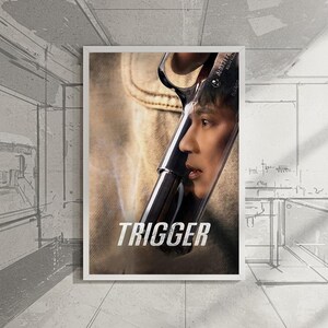 Pode incluir: Um poster emoldurado com um close-up de uma arma de fogo com o rosto de uma pessoa refletido no cano. A palavra "TRIGGER" é impressa em letras brancas na parte inferior da imagem. O fundo é de cor neutra.