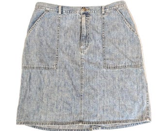 May include: Light blue denim skirt with two front pockets and a button closure. The skirt has a classic, casual style, with a faded wash and visible stitching details. The skirt is a knee-length design.