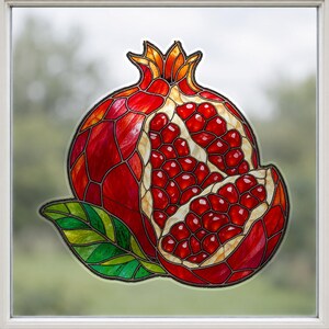May include: A stained glass window cling featuring a pomegranate with a deep red exterior and exposed ruby-red seeds. The design includes a green leaf at the base and a golden-orange crown at the top, all outlined in dark lead-like lines.