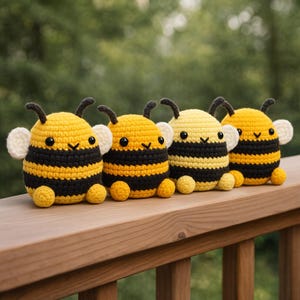 May include: Four handmade crochet bees in a row. Each bee has a yellow body with black stripes, small black eyes, and white wings. They are sitting on a wooden surface with a blurred green background.